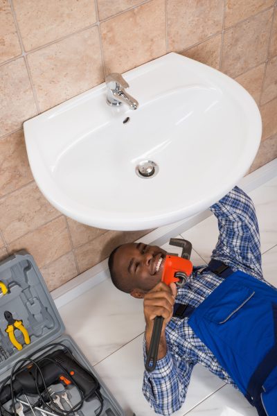 Happy Young African Male Plumber Fixing Sink In Bathroom