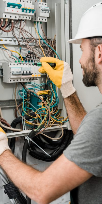 side view of electrician repairing electrical box and using screwdriver in corridor