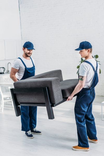 two movers in uniform transporting furniture in apartment