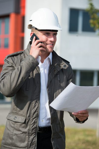 Homme en casque de chantier parlant au téléphone et tenant des plans